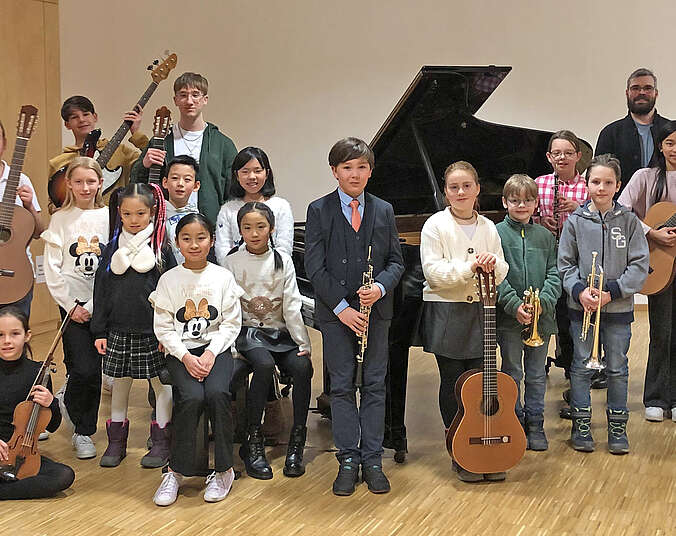 Junge Musikerinnen und Musiker stehen vor einem schwarzen Flügel mit ihren Lehrkräften